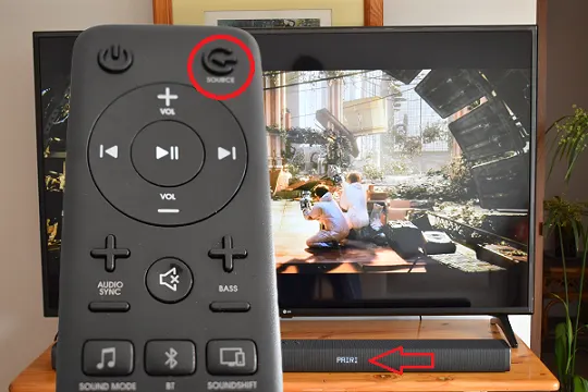 L'immagine mostra un telecomando della soundbar JBL con il pulsante source evidenziato.